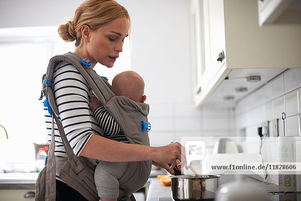 Frau beim Kochen in der Küche  Baby im Tragetuch an den Körper geschnallt