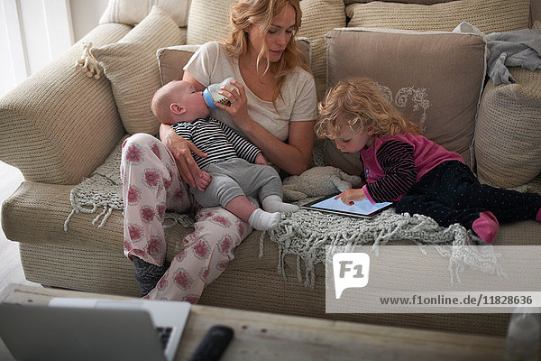 Mutter füttert Baby-Sohn und hilft Tochter mit digitalem Tablett