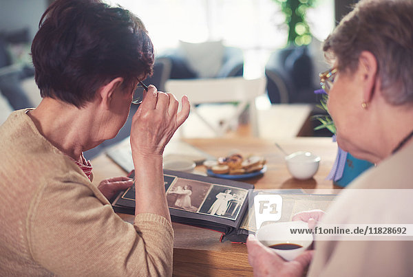 Über-Schulter-Ansicht zweier älterer Frauen beim Betrachten des Fotoalbums auf dem Tisch
