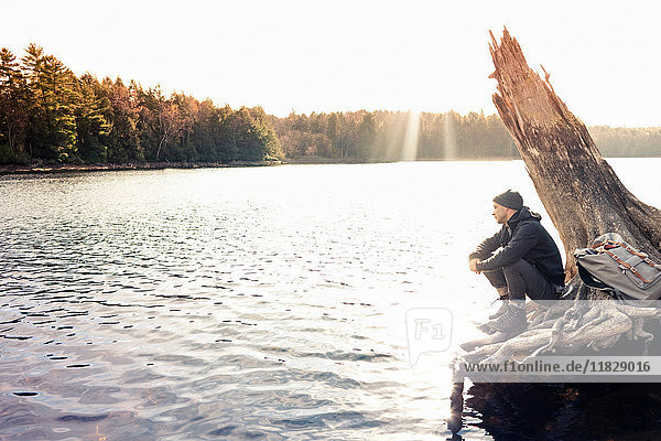 Man sitting on boulder by still lake