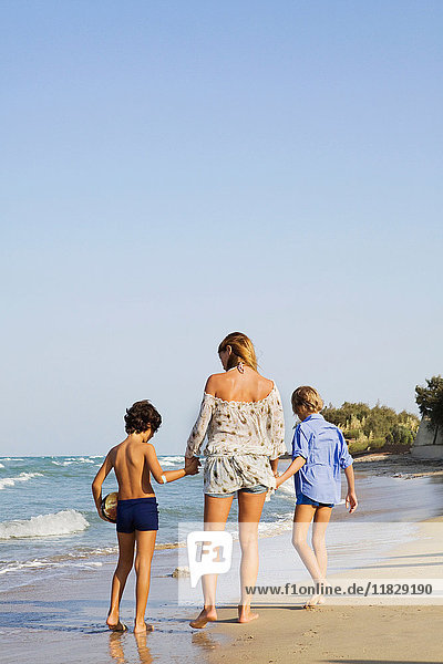 Frau geht mit Kindern am Strand spazieren