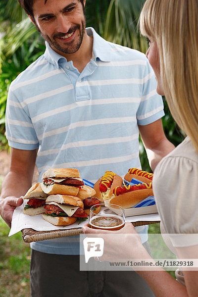 Mann hält Tablett mit Burgern und Hot Dogs