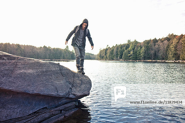 Man walking on boulder by still lake
