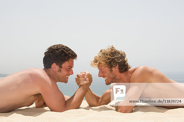 Two young men arm wrestling on the beach