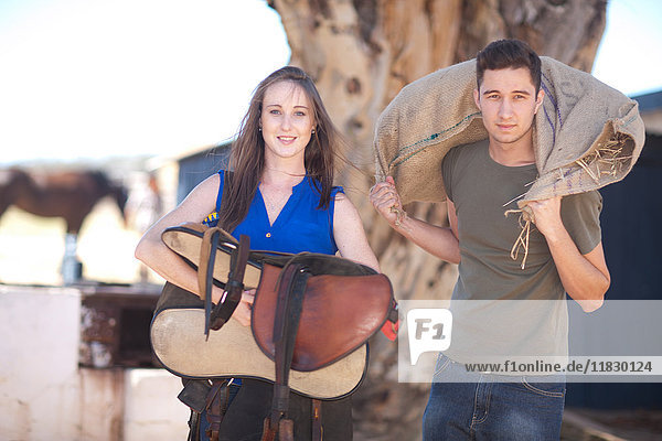 Young couple carrying saddle and sack of hay