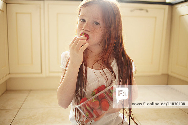 Mädchen isst Erdbeere auf Küchenboden