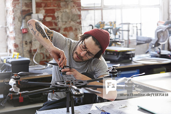 Männlicher Designer mit Tätowierungen und Drohne in der Werkstatt