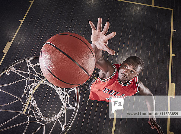 Overhead-Ansicht junger männlicher Basketballspieler, der springt, um den Ball auf die Basketballfelge zu prallen.