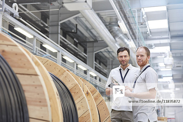Portrait smiling male supervisors with clipboard talking in fiber optics factory