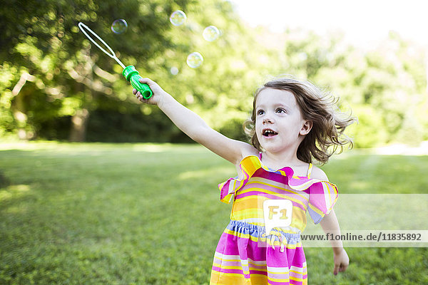 Preschool girl playing with bubble wand in summer yard