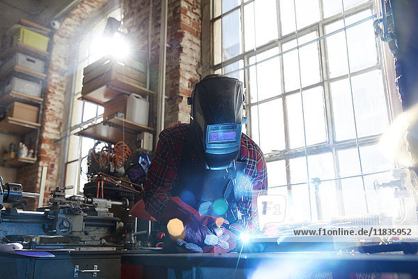 Welder welding with welding mask and torch in workshop