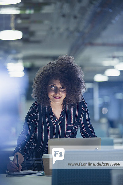 Portrait lächelnde  selbstbewusste Geschäftsfrau  die spät am Laptop im dunklen Büro arbeitet.