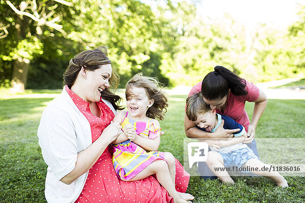 Lesbian mothers playing  tickling children in summer grass yard