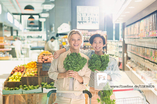 Portrait smiling young female friends holding kale in grocery store market
