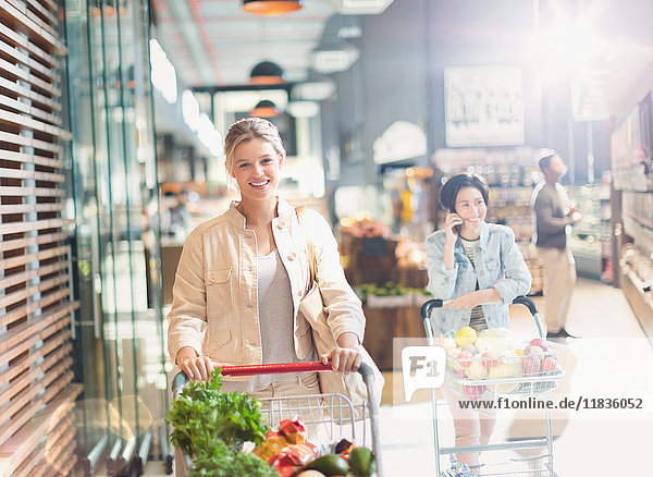Portrait smiling young woman with shopping cart in grocery store market