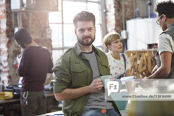 Portrait confident young male designer drinking coffee in workshop