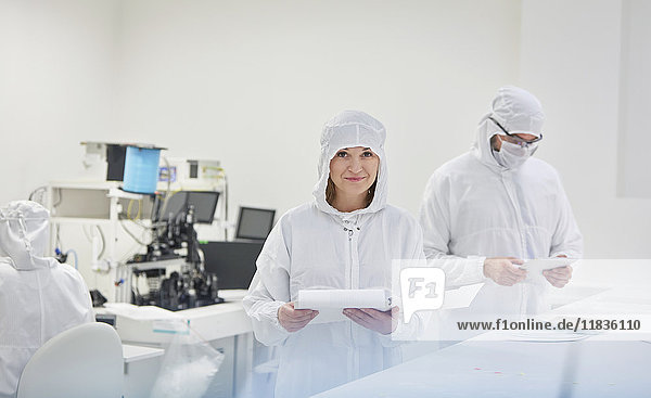 Portrait smiling female engineer in protective suit with paperwork in fiber optics research and testing laboratory