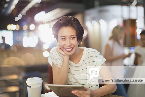 Porträt einer lächelnden jungen Frau  die ein digitales Tablet benutzt und in einem Café Kaffee trinkt
