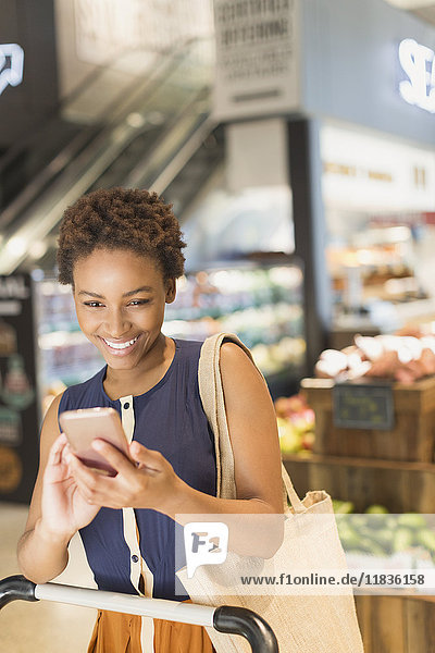 Smiling young woman using cell phone in grocery store market
