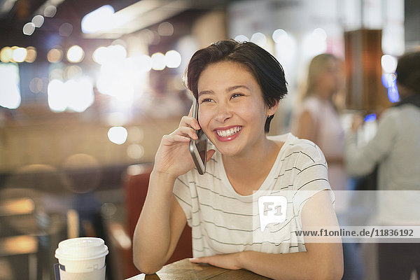 Lächelnde junge Frau  die in einem Café mit ihrem Handy telefoniert