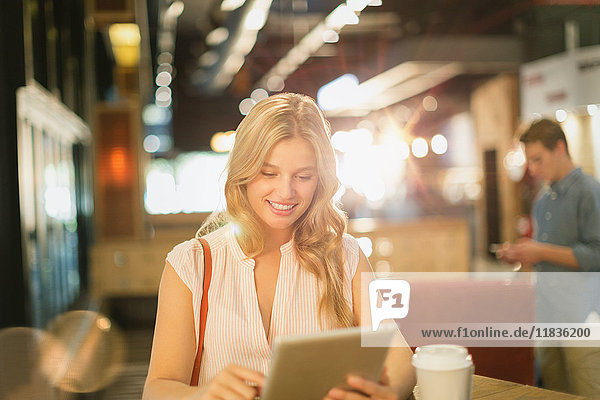 Lächelnde junge Frau  die ein digitales Tablet benutzt und Kaffee in einem Café trinkt
