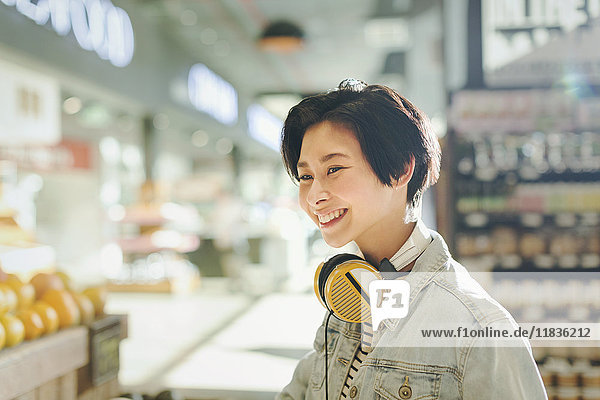 Smiling young woman with headphones grocery shopping in market