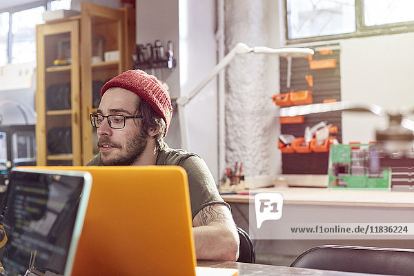 Male designer working at laptop in workshop