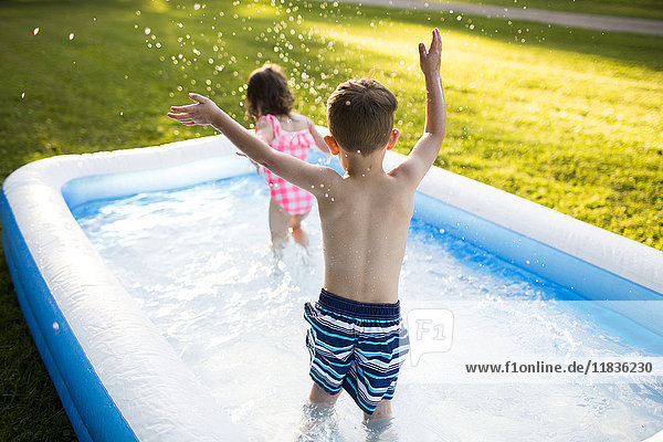 Preschool brother and sister playing and splashing in inflatable swimming pool