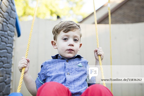 Portrait serious preschool boy swinging on swing