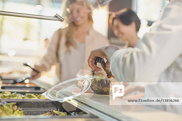 Young woman serving salad at salad bar in grocery store market