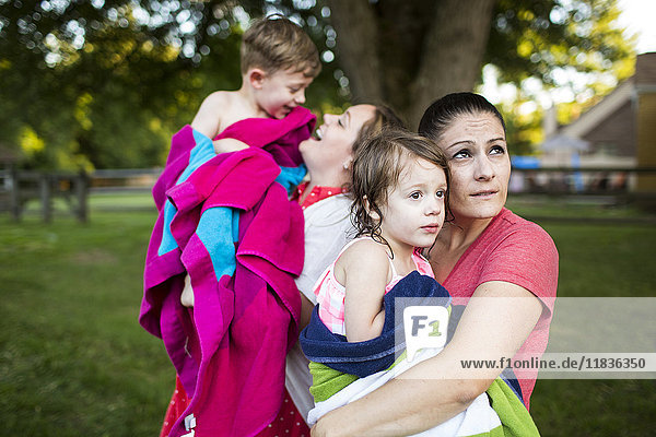 Lesbian mothers holding wet children wrapped in a towel in summer yard