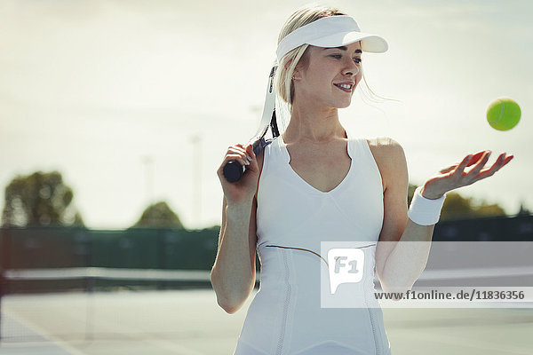 Lächelnde junge Tennisspielerin mit Tennisschläger und Tennisball auf dem Tennisplatz