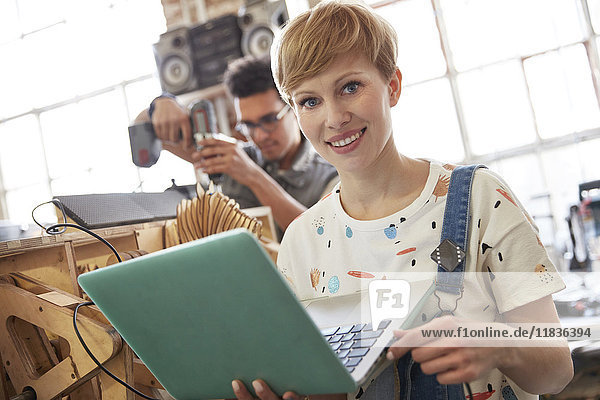 Portrait smiling female designer using laptop in workshop