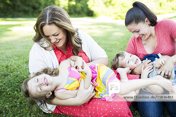 Playful lesbian mothers playing  tickling children in grass