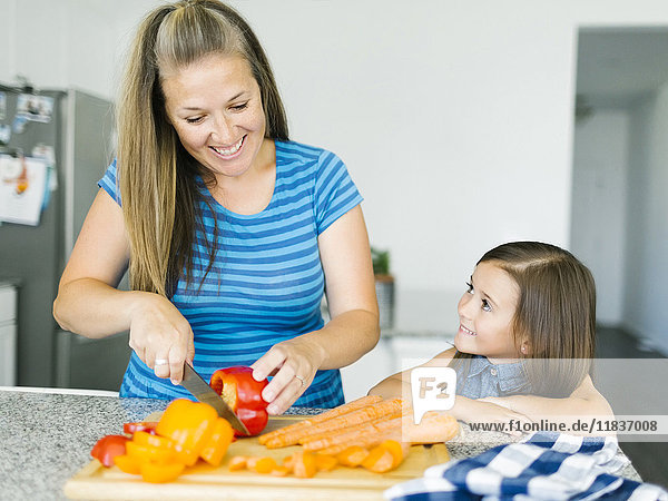 Mutter schneidet Gemüse mit Tochter (6-7) in der Küche