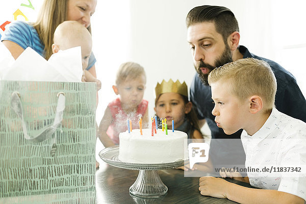 Familie mit vier Kindern (6-11 Monate  2-3  6-7) beim Ausblasen von Kerzen auf der Geburtstagstorte
