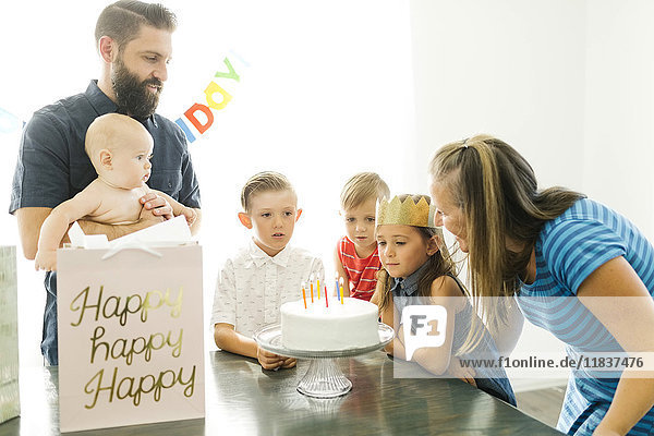 Eltern mit Kindern (6-11 Monate  2-3  6-7) betrachten ihre Tochter (6-7) beim Ausblasen von Geburtstagskerzen