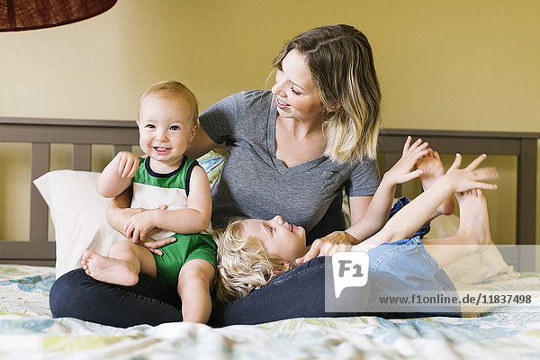 Mutter mit Söhnen (12-17 Monate  4-5) auf dem Bett sitzend