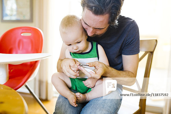 Vater schneidet die Fingernägel seines Sohnes (12-17 Monate)
