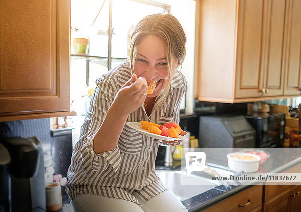 Frau in Küche isst Obstsalat