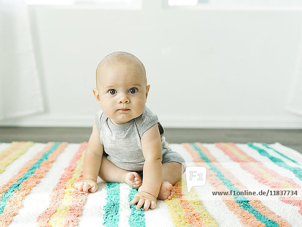 Porträt eines kleinen Jungen (6-11 Monate) auf einem bunten Teppich sitzend