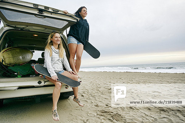 Kaukasische Frauen in einer Autoluke am Strand mit Skateboards