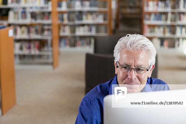 Lächelnder hispanischer Mann am Computer in einer Bibliothek