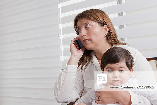 Hispanische Mutter hält ihren kleinen Jungen und spricht mit dem Handy