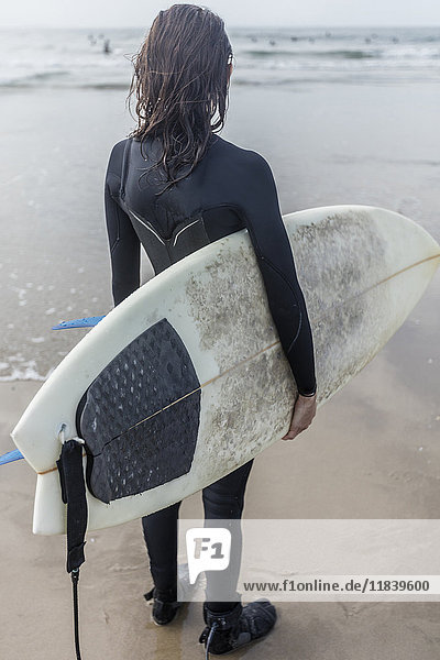 Kaukasische Frau steht am Strand und hält ein Surfbrett