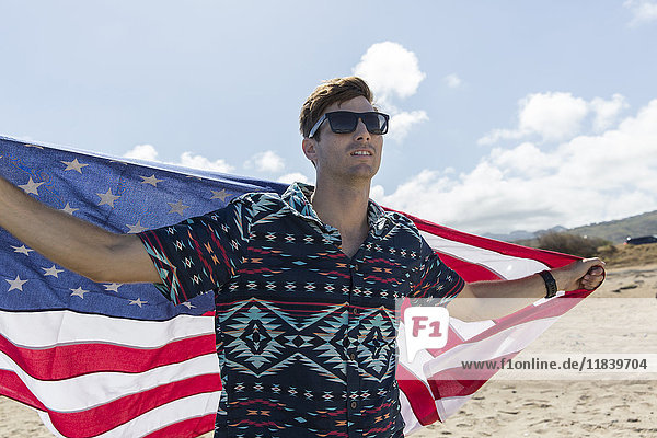 Kaukasischer Mann hält amerikanische Flagge am Strand