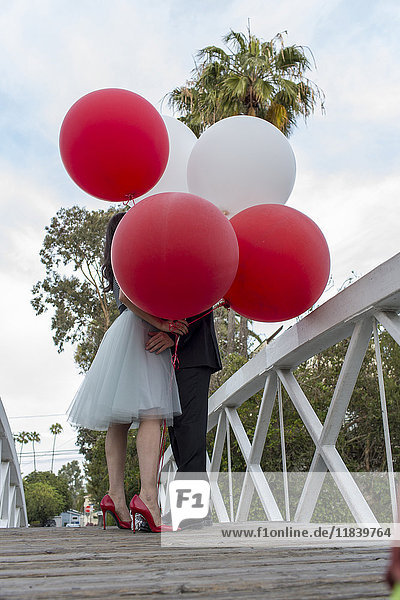 Paar auf Brücke küsst sich hinter Ballons