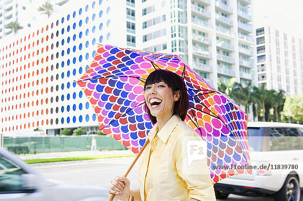 Lachende gemischtrassige Frau mit Regenschirm in der Stadt