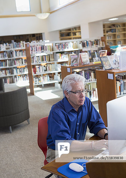 Ernster hispanischer Mann  der einen Computer in einer Bibliothek benutzt