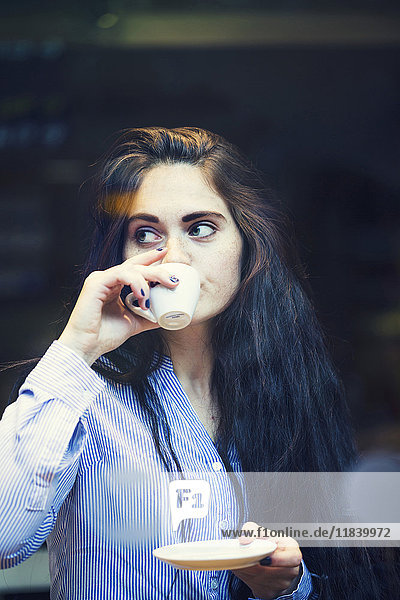 Neugierige kaukasische Frau schlürft Kaffee im Freien